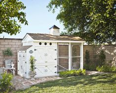 a small white shed sitting in the middle of a yard next to a brick wall