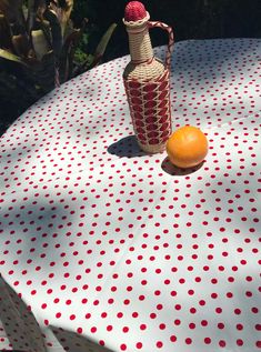 an orange sitting on top of a white table cloth next to a bottle with red dots