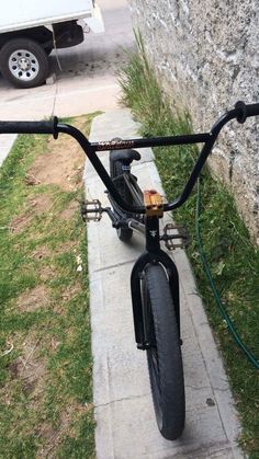 a bicycle parked on the sidewalk next to a stone wall with grass growing in it