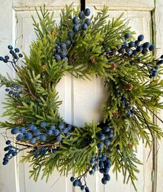 a wreath with blue berries and pine cones hanging on a door