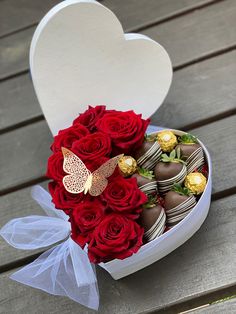 a heart shaped box filled with red roses and chocolate covered strawberries on top of a wooden table