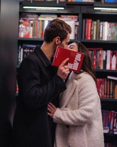 a man and woman kissing in front of a bookcase with books on the shelves