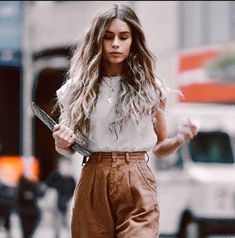 a woman walking down the street with her hair blowing in the wind and holding a cell phone