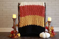 a crocheted blanket sitting on top of a wooden chair next to two candles