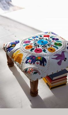 a colorfully decorated ottoman sitting on top of a white floor next to a stack of books