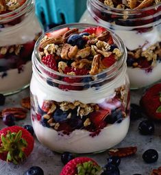 three glass jars filled with yogurt, granola and berries on a table