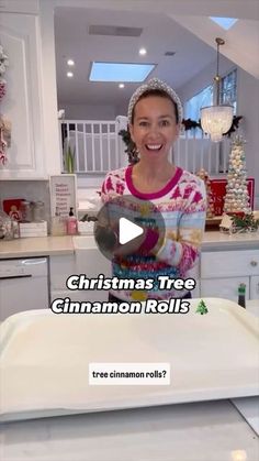 a woman in a christmas tree sweater is holding a tray with cinnamon rolls on it