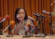 a woman sitting at a table in front of microphones and talking on the phone