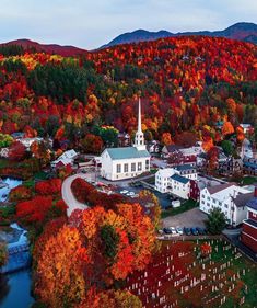 an aerial view of a small town surrounded by trees with autumn foliage in the background