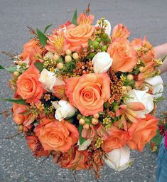 an orange and white bridal bouquet being held by a woman's hand on the street