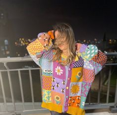 a woman standing on top of a balcony wearing a colorful sweater and leggings