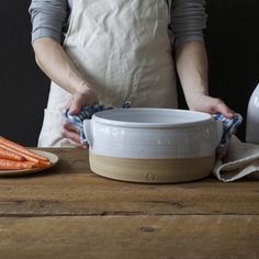 a person in an apron holding a bowl with carrots next to it on a wooden table