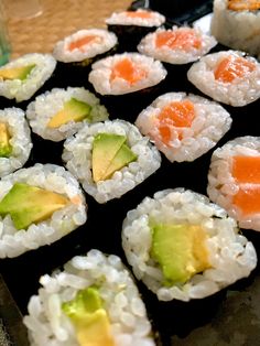 sushi rolls with avocado, carrots and other toppings on a black tray