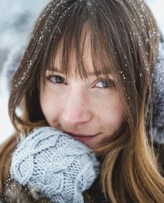 a woman with long hair wearing a gray hat and mittens is posing for the camera