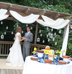 a bride and groom standing in front of a table with desserts on top of it