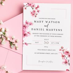 a wedding card with pink flowers on it next to some white and pink envelopes