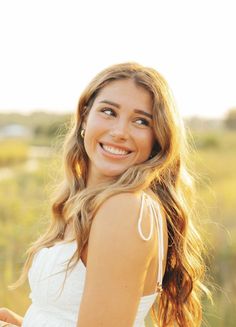 a beautiful young woman standing in front of a field smiling and looking at the camera