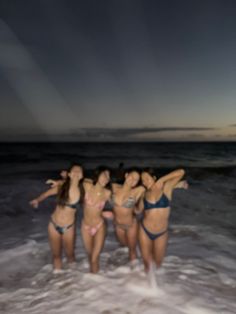 four women in bikinis are standing in the water at the beach with their arms around each other