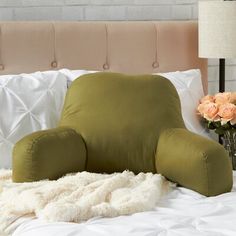 a green chair sitting on top of a bed next to a vase filled with flowers