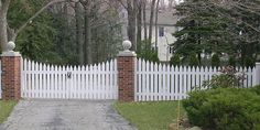 a white picket fence and gate in front of a house with trees on either side