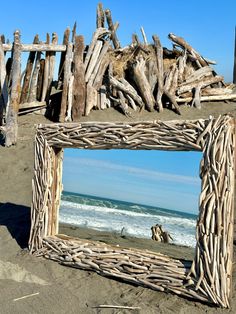 a wooden frame sitting on top of a sandy beach next to the ocean with driftwood sticking out of it