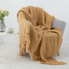 a chair with a blanket draped over it next to a vase and flowers on a table