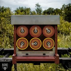 an old fashioned machine sitting in the middle of some tall grass and trees, with four dials on each side