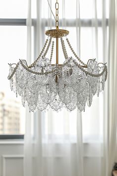 a chandelier hanging from a ceiling in front of a window with white curtains