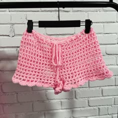 a pink crocheted shorts hanging on a rack against a white brick wall with a black hanger