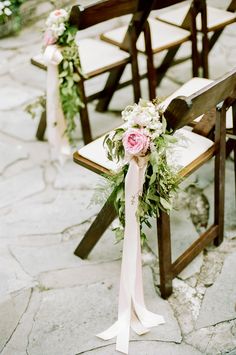 two wooden chairs with flowers and greenery tied to the back one chair is empty