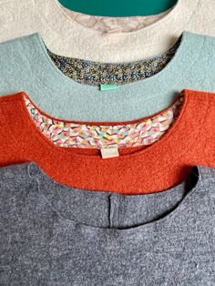 four sweaters are lined up on a table top, one is gray and the other is orange