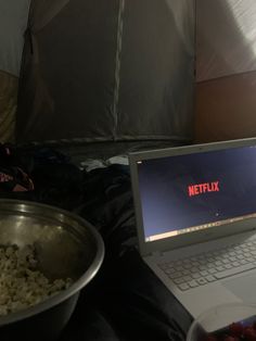 an open laptop computer sitting on top of a table next to a bowl of popcorn