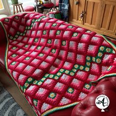 a crocheted blanket is sitting on a red leather couch in a living room