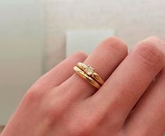 a person's hand holding a gold ring with two small diamonds on the side