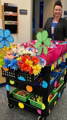 a woman standing next to a cart filled with lots of flowers and plastic bins