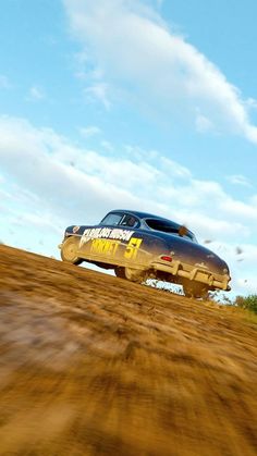 a car driving down a dirt road in front of a blue sky with white clouds