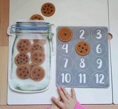 a child's hand next to a mason jar with buttons and numbers on it