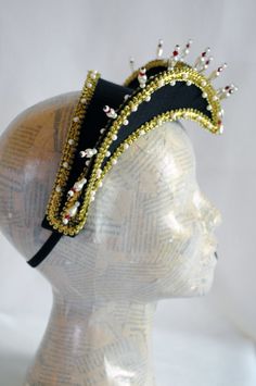 This royal Tudors inspired attifet headdress will make an excellent addition to your historical costume. It is covered with black silk shantung and embellished with golden braided trimming all around the edges.This unique piece wouldn't be complete without all those wonderful pearl bead details that add some royal flair to it's elegance. Choose between only pearl decoration or a combination of pearl beads and small red crystals to add just a pop of color. The headpiece is very light and comforta Carnival Costume Headpiece With Round Crown, Traditional Costume Hats And Headpieces For Carnival, Tall Crown Costume Hats And Headpieces For Carnival, Structured Crown Costume Hats And Headpieces For Carnival, Costume Hats With Structured Crown For Carnival, Carnival Costume Headpiece With Structured Crown, Carnival Costume Party Hat With Structured Crown, Tall Crown Headpiece For Carnival Costume, Carnival Crown Costume Hats And Headpieces