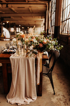 a table with flowers and candles on it in an old warehouse or industrial building is set up for a wedding reception