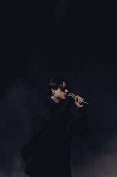 a male in a black jacket is holding a microphone and standing on the stage with his hand up to his mouth