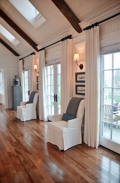 a living room filled with white furniture and wooden flooring next to two large windows