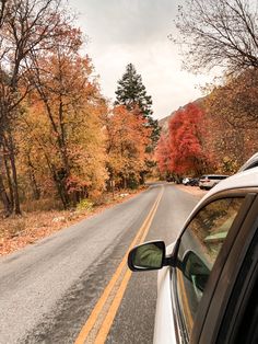 a car is parked on the side of the road in front of trees with orange and yellow leaves