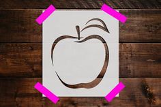 an apple cut out on top of a piece of paper with pink tape around it