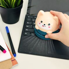 a person is holding a small piggy bank near a laptop computer and pen on a desk