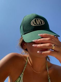 a woman wearing a green hat covering her face with her hands and looking at the sky