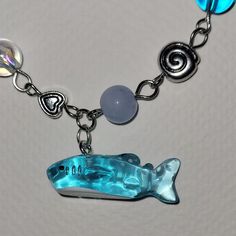 a blue glass fish charm on a silver plated chain with other charms around it