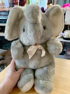 an elephant stuffed animal sitting on top of a wooden table next to a person's hand