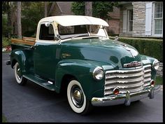 an old green truck parked in front of a house