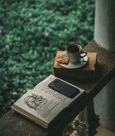 a cup of coffee sitting on top of a book next to a cell phone