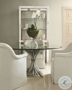 a glass table with chairs around it and a vase on the top, in front of two white chairs